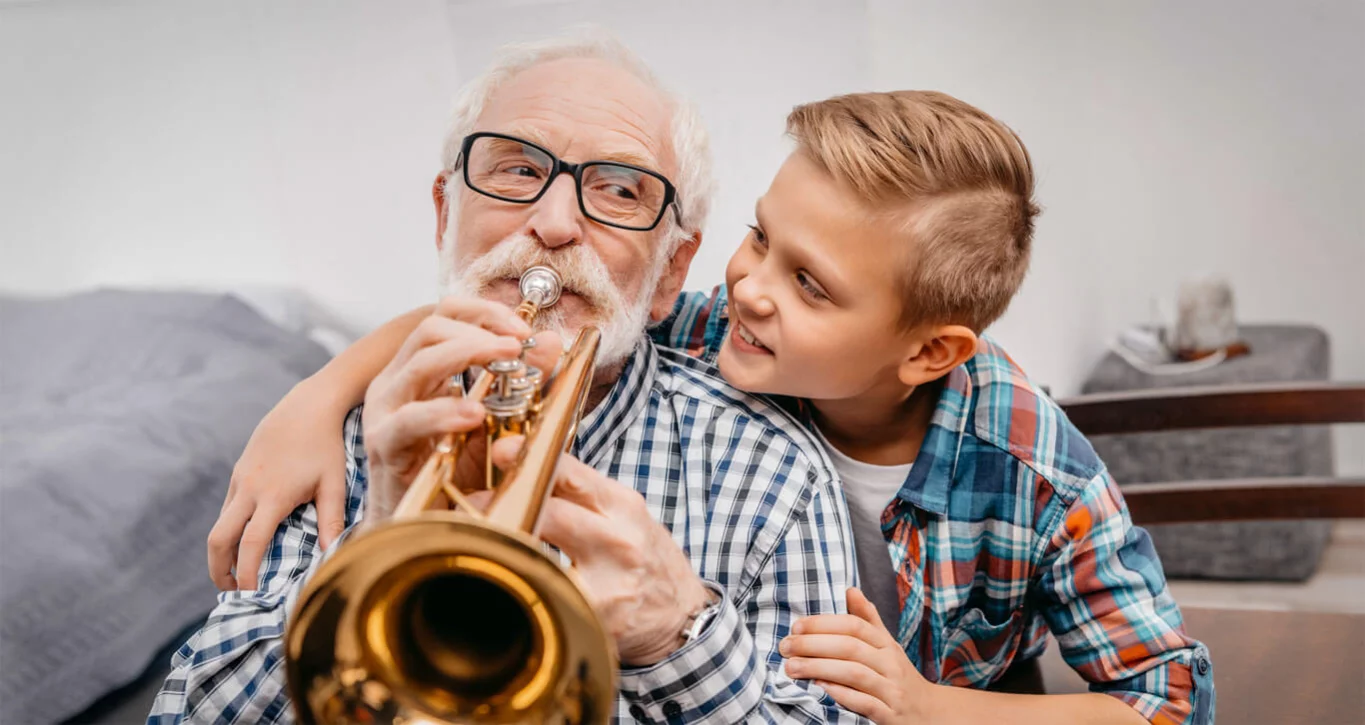 Der Enkel schaut seinem Großvater beim Trompete-Spielen über die Schulter. 